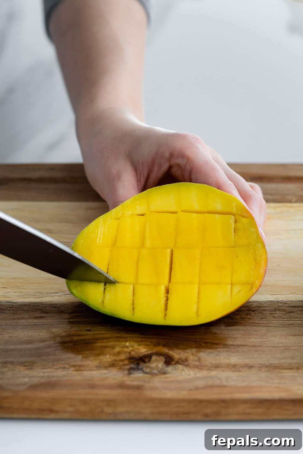 Knife slicing cubes in mango flesh, showing the grid pattern before inverting