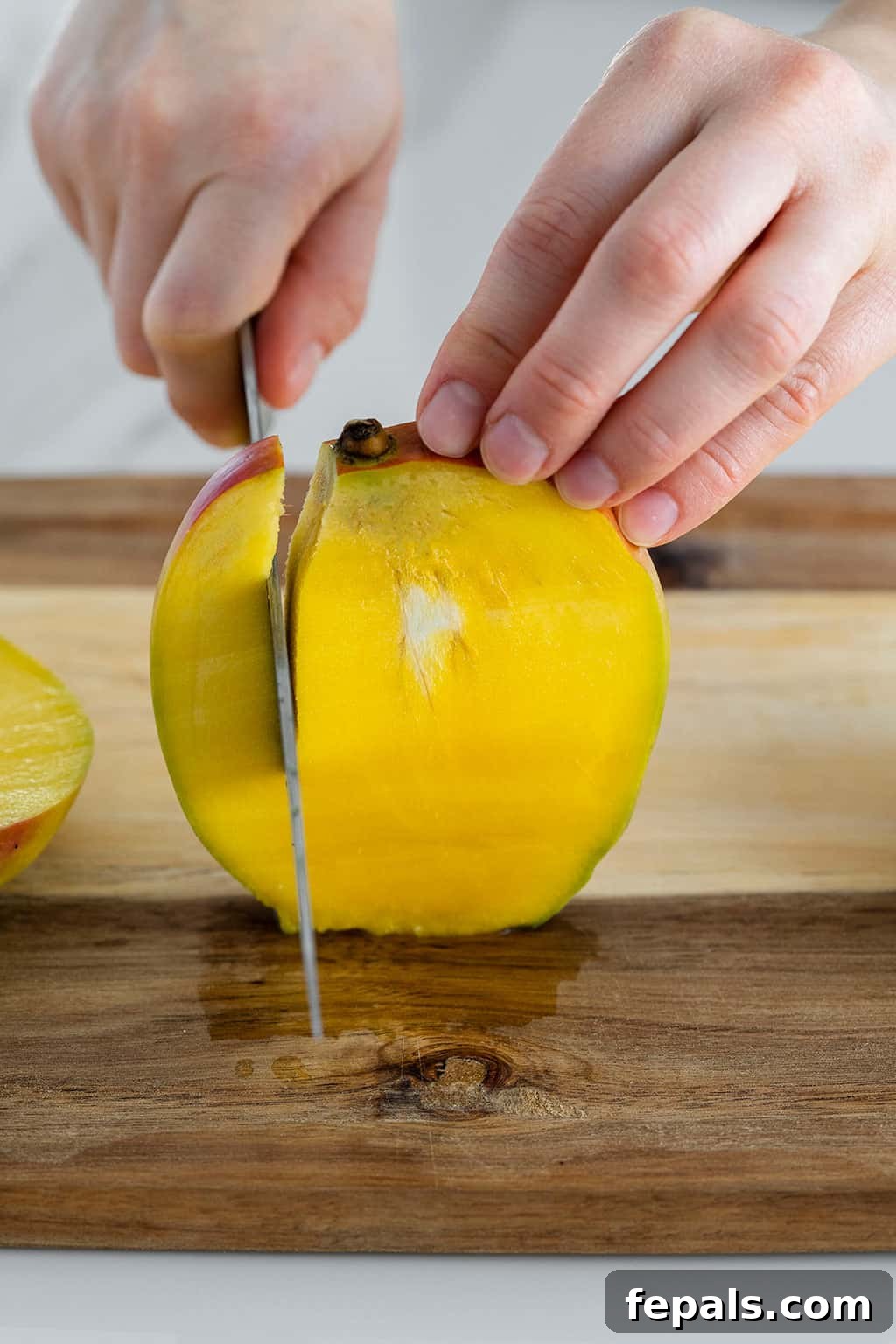 Side view of a mango being sliced with a knife, demonstrating the first cut near the pit