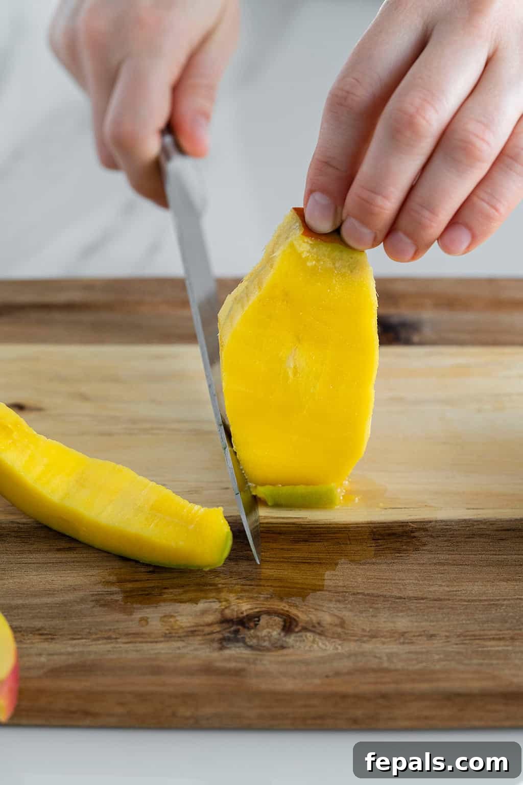 Side shot of mango flesh being scored with a knife, illustrating cuts without piercing the skin