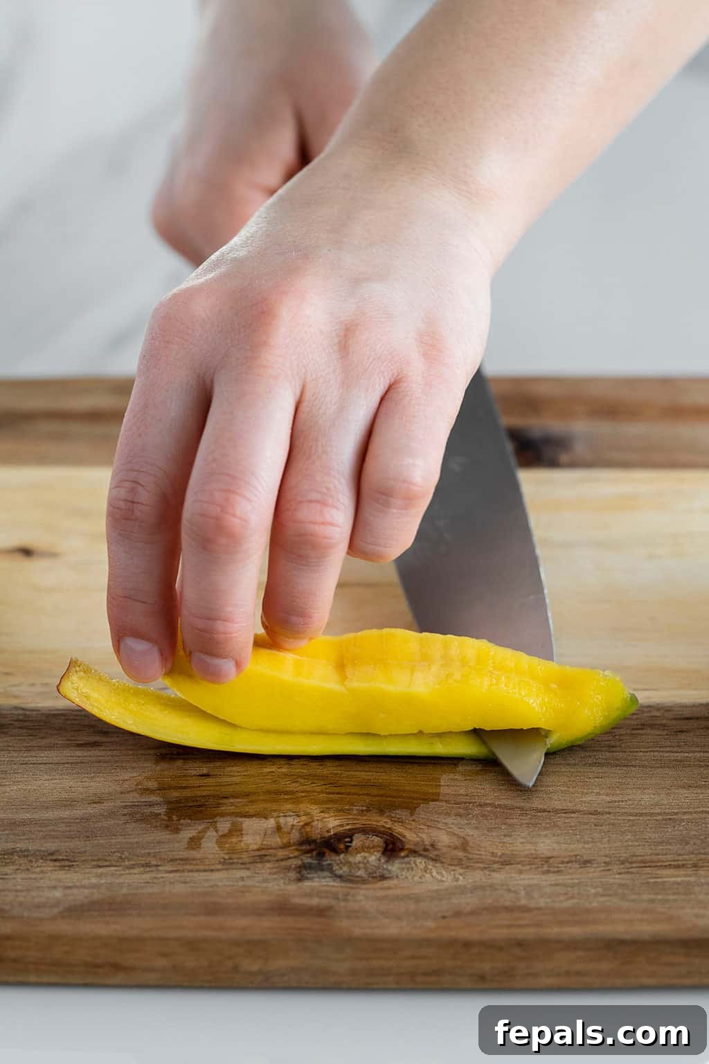 Mango slice on a cutting board with a knife carefully separating the flesh from the skin