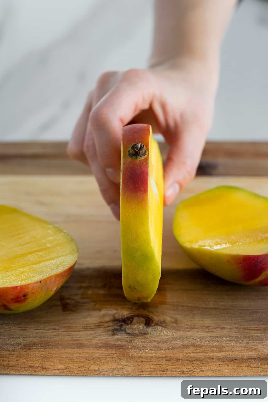 Hand holding mango seed stem side up, showing the remaining pit after cheeks are removed
