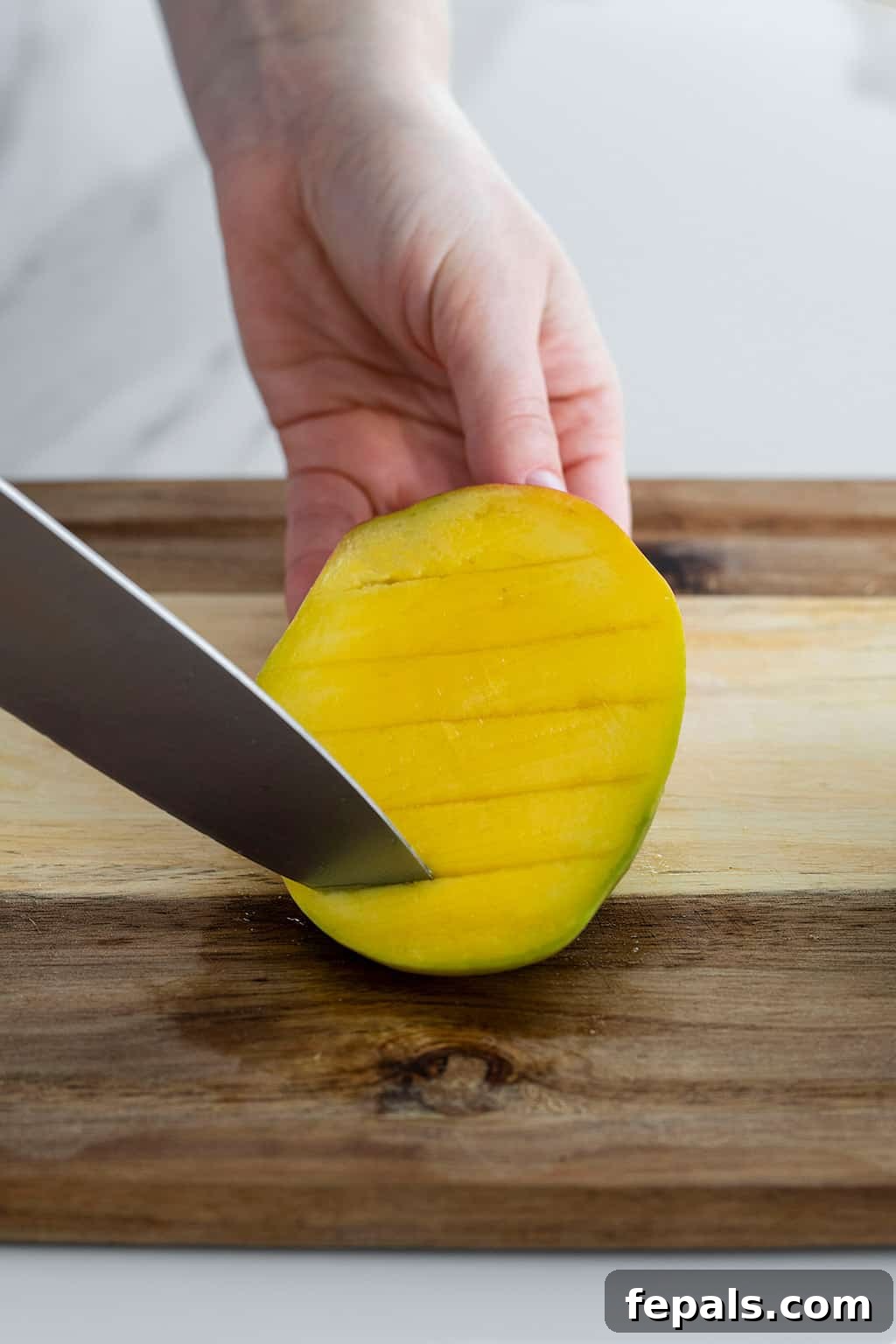 Knife slicing flesh of mango, illustrating the scoring process for cubes