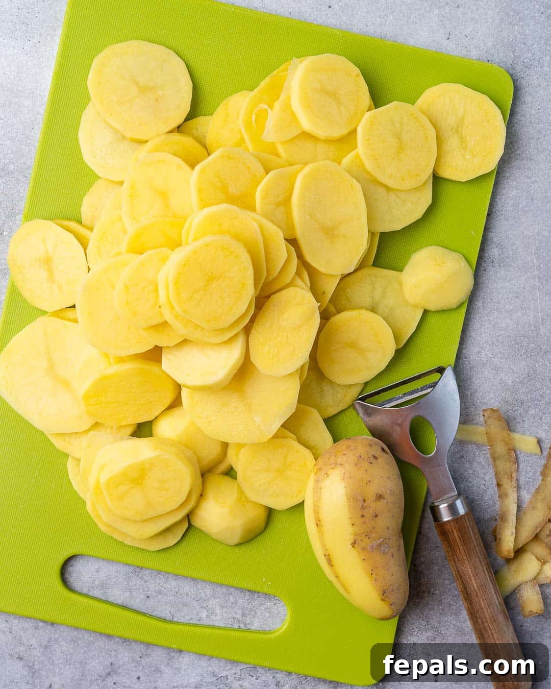 Effortless Cheesy Potato Gratin 5 Thinly sliced potatoes arranged on a green cutting board, ready for preparation.