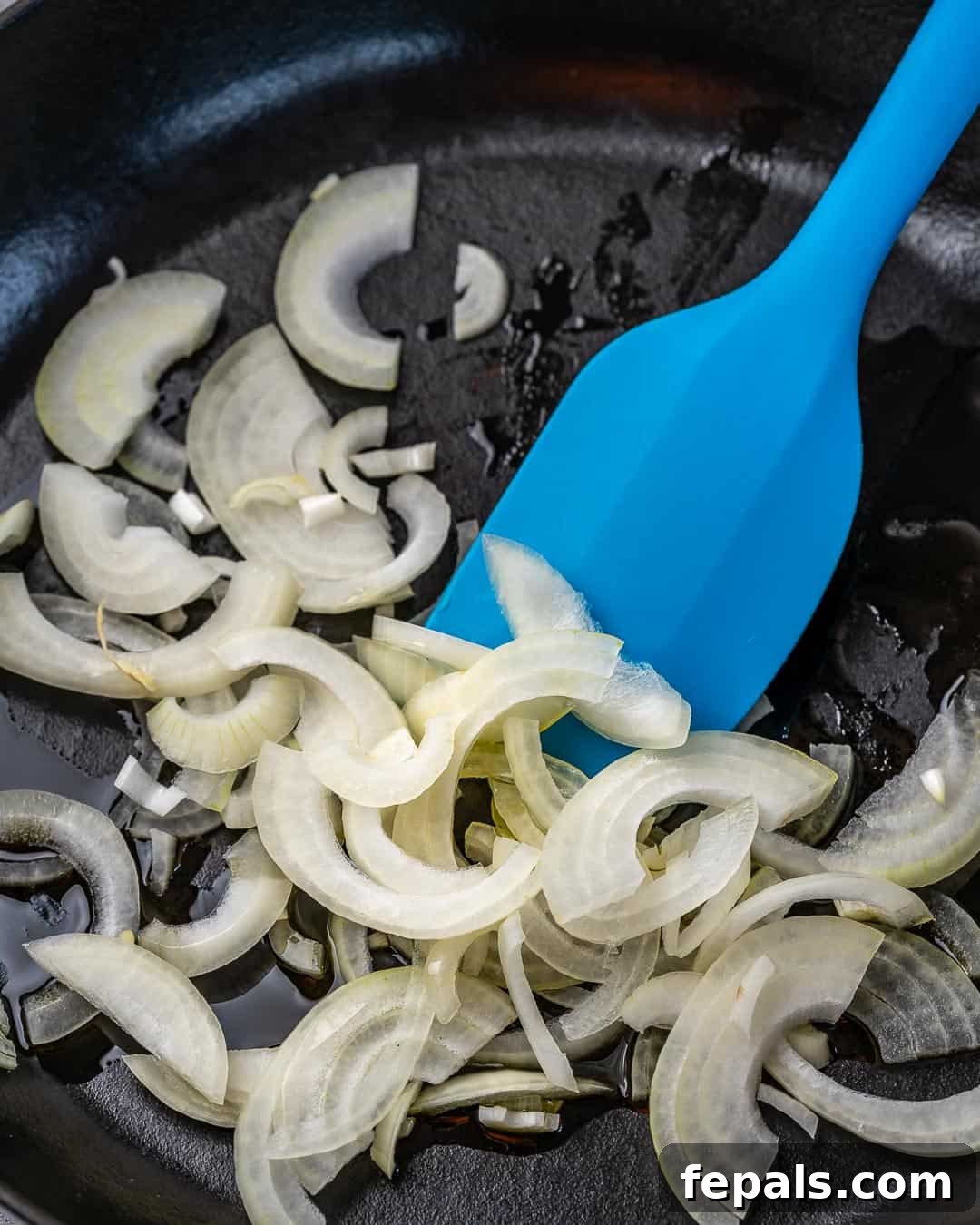 Effortless Cheesy Potato Gratin 6 Thinly sliced onions sautéing in a black skillet on a stovetop.