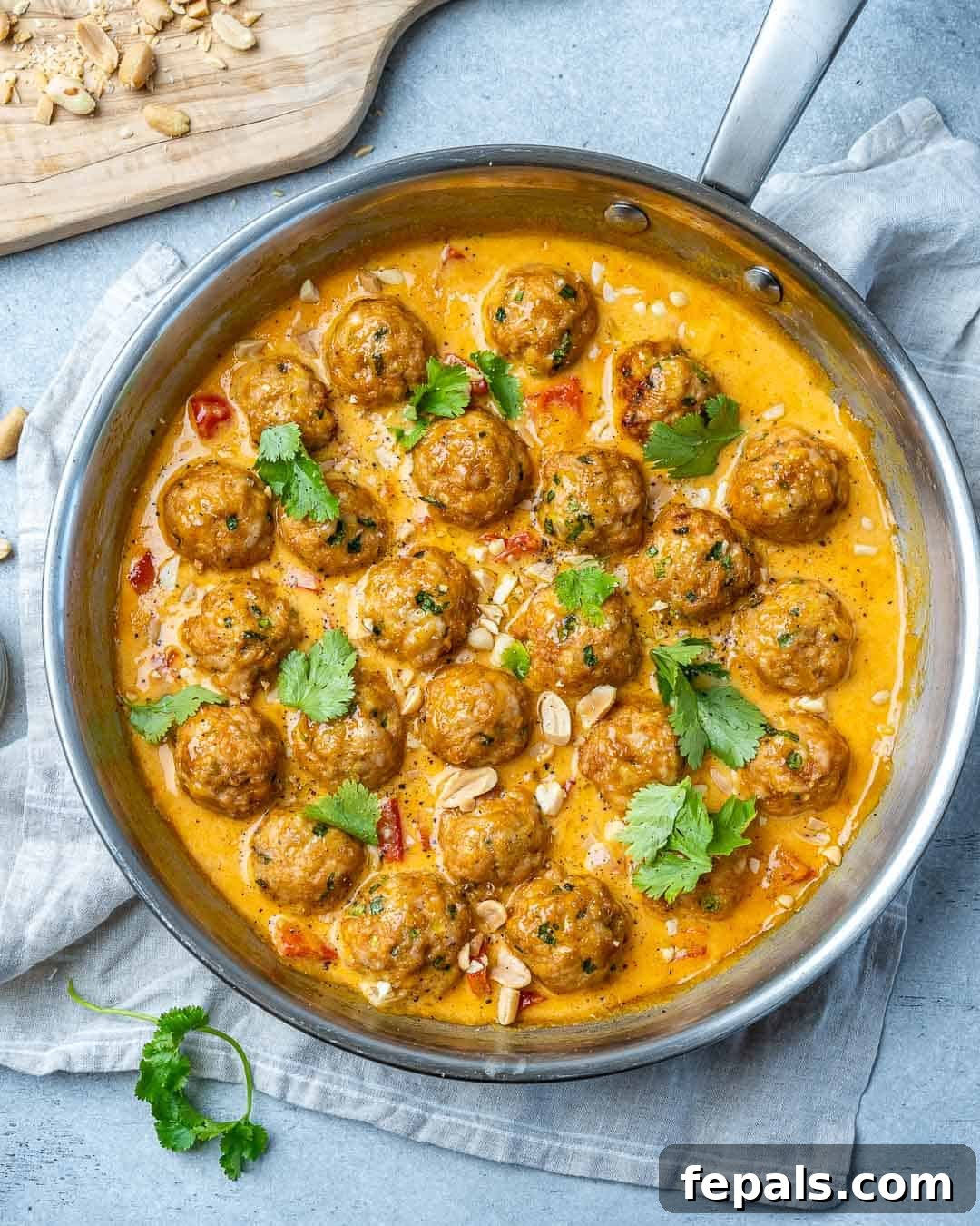 Turkey meatballs in a curry sauce in a stainless steel round pan with cilantro garnish.