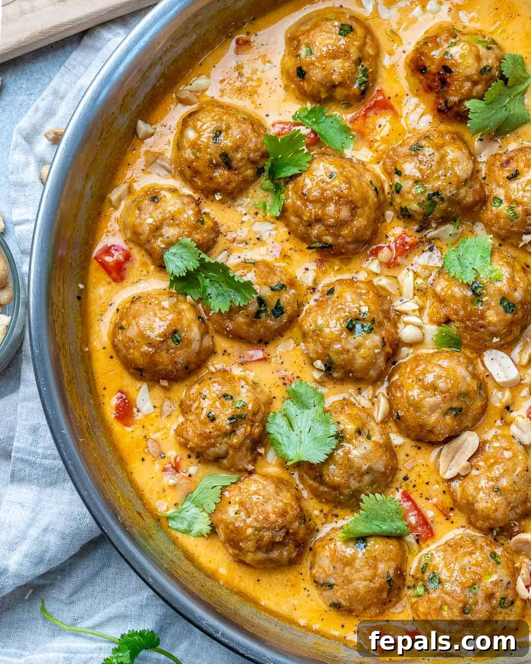 Turkey meatballs in a curry sauce in a stainless steel round pan with cilantro and chopped peanuts garnish.