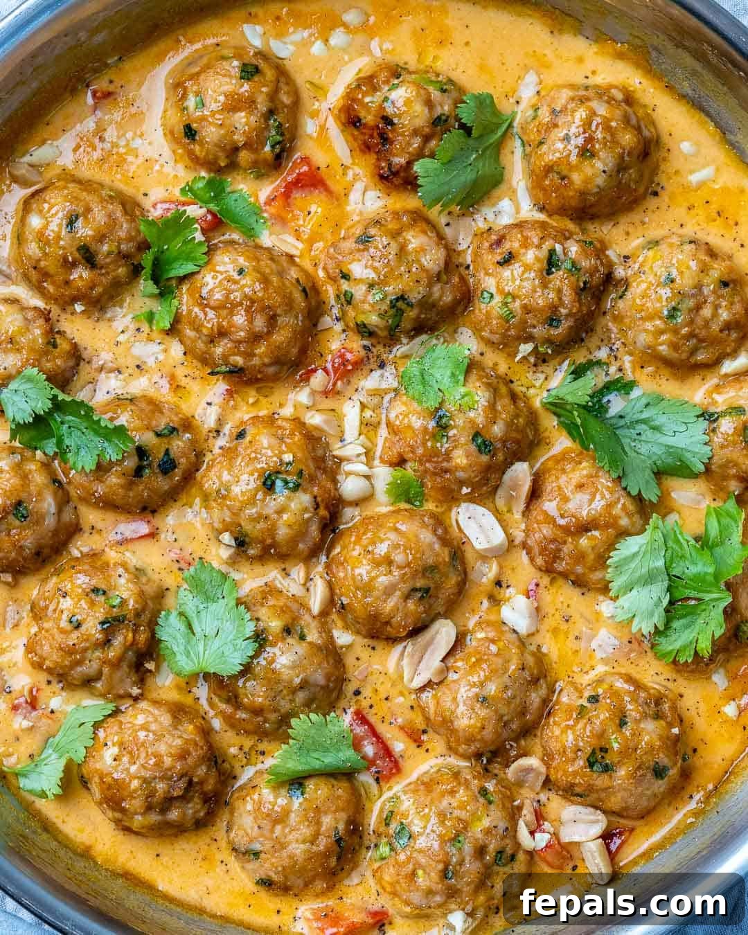 Turkey meatballs in a curry sauce in a stainless steel round pan with cilantro and chopped peanuts garnish.