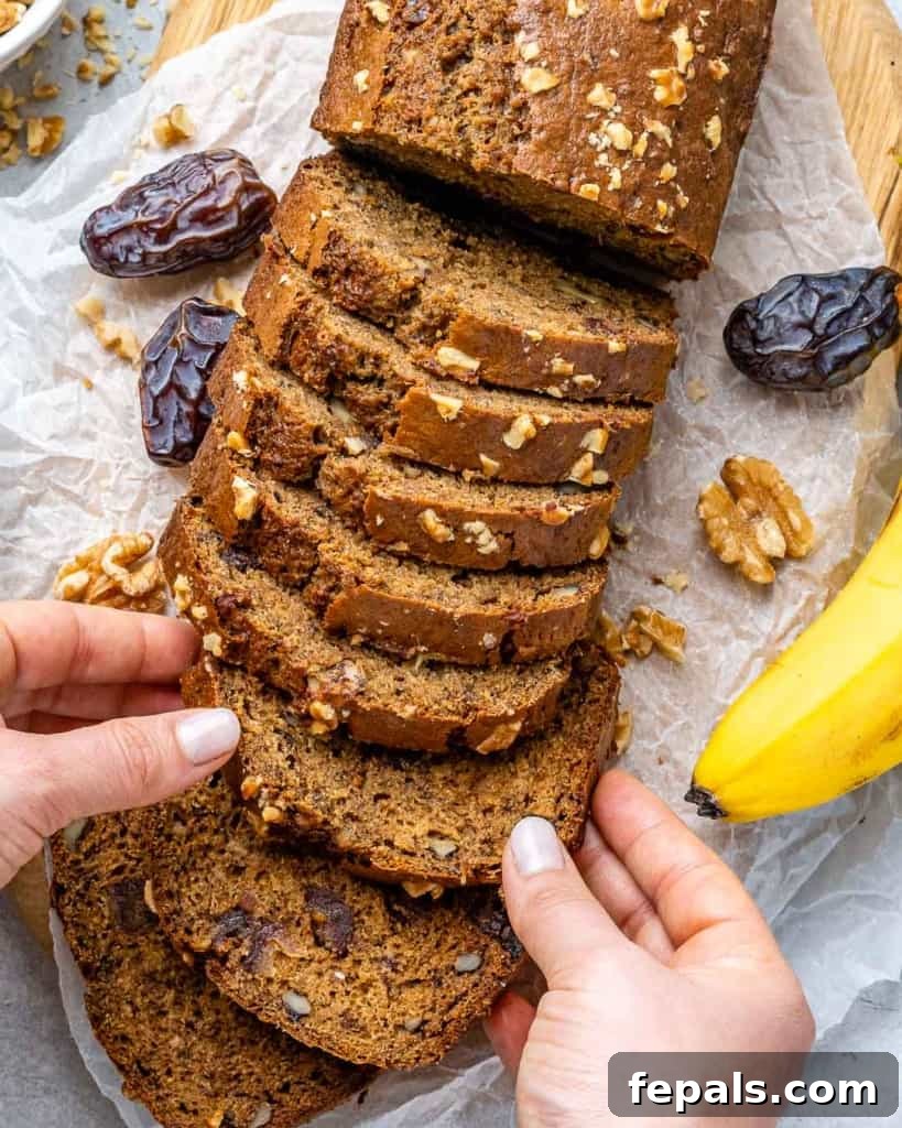 A hand holding a perfectly sliced piece of banana date nut bread, showcasing its moist texture and rich inclusions.