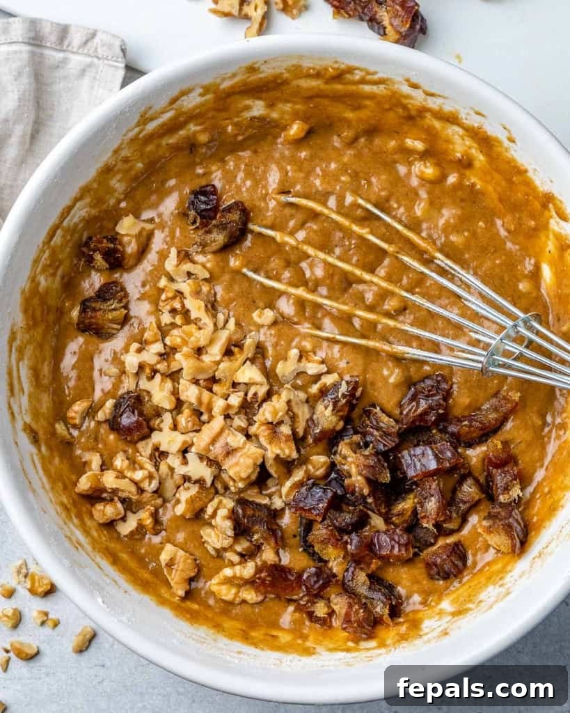 Close-up of chopped nuts and dates resting on top of the banana bread batter in a white mixing bowl.