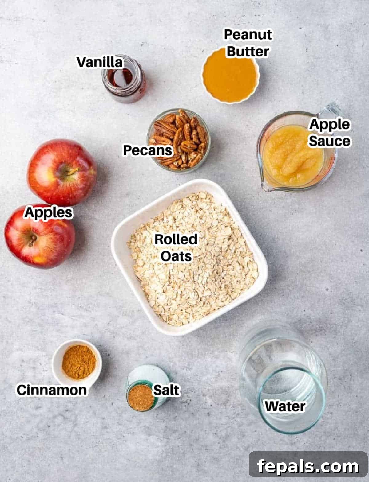 Nutty Oatmeal Morning Fuel 4 A flat lay of ingredients laid out on a white surface, including oats, peanut butter, apples, cinnamon sticks, and maple syrup.