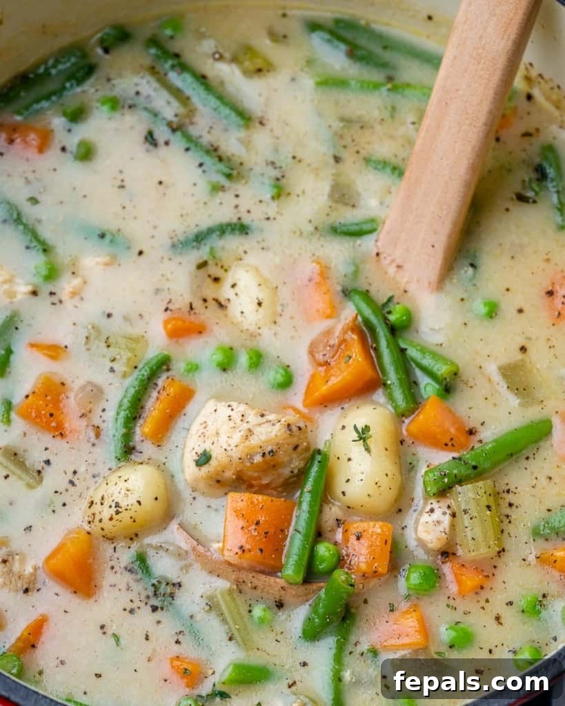 Close-up of a pot filled with rich chicken and gnocchi soup, highlighting the vegetables and gnocchi texture.