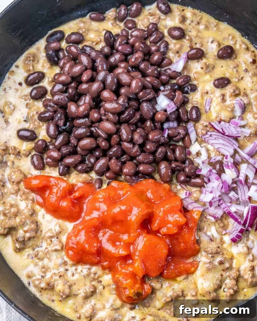 Rancher's Rustic Queso 6 Top view of colorful ingredients, including diced tomatoes, black beans, and chopped onions, being mixed into a rich, cheesy ground beef base for the delicious queso