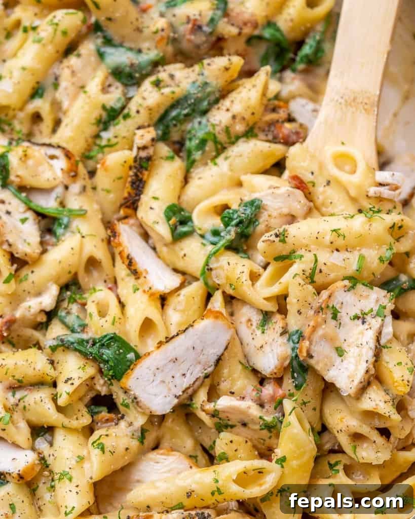 Creamy Chicken Spinach Pasta 3 Close view of chicken, spinach, and pasta with wooden spoon