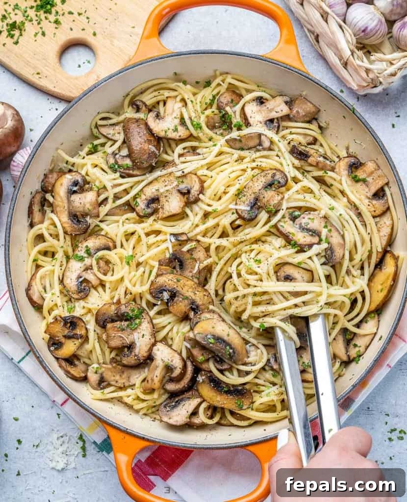 Tongs grabbing savory mushroom garlic spaghetti from an orange skillet, ready to serve.
