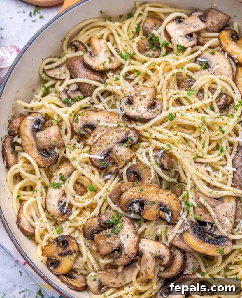 A close-up, mouth-watering view of garlic mushroom spaghetti perfectly coated in sauce, nestled in a skillet.