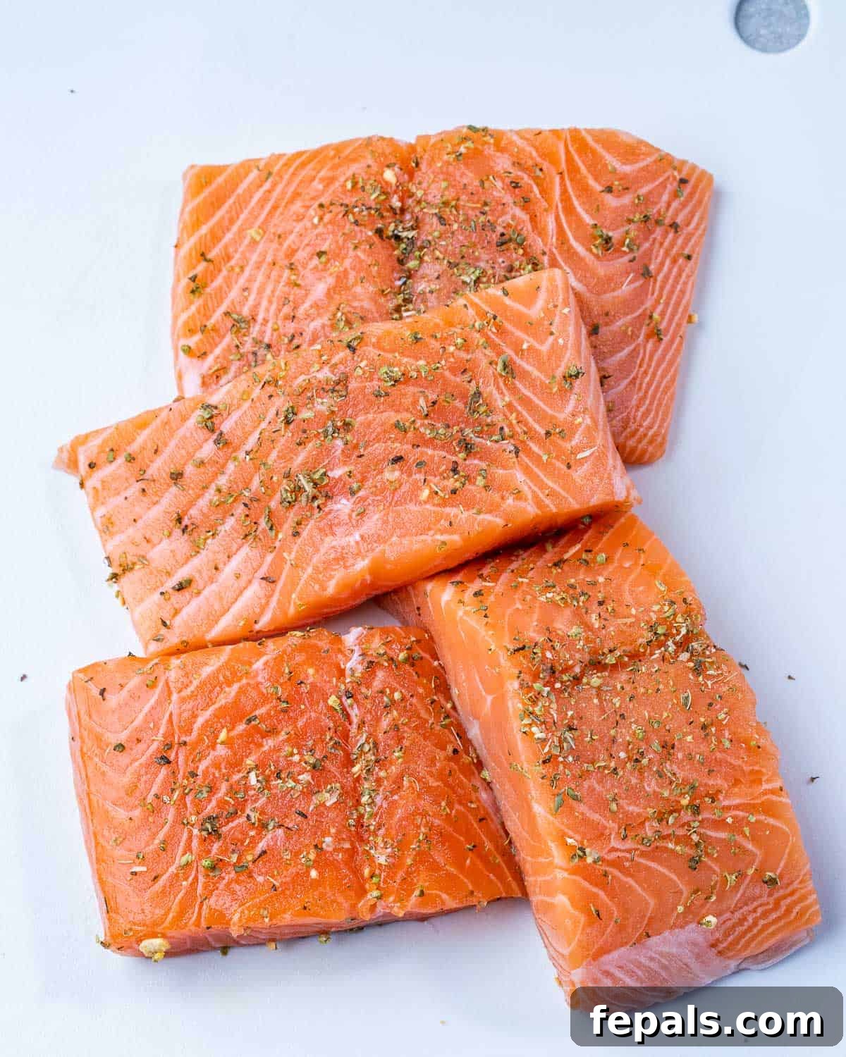 Zesty Salmon Piccata 5 Four fresh salmon fillets perfectly seasoned with herbs and spices on a wooden cutting board, ready for cooking.