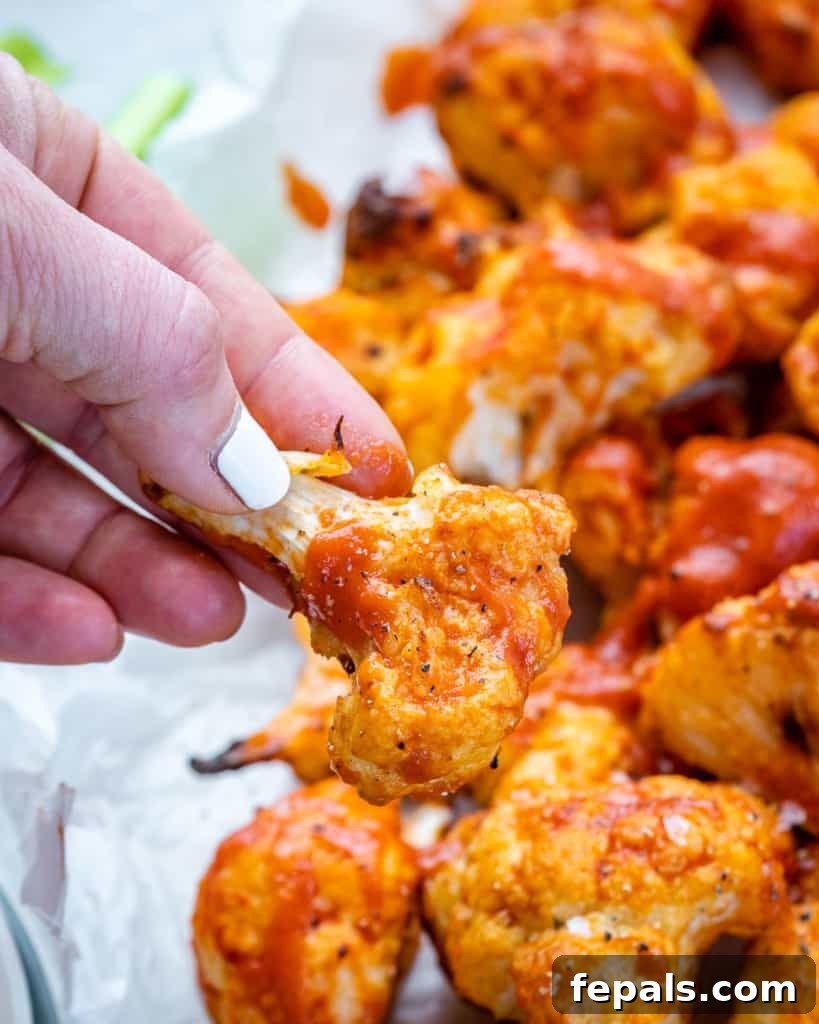 Hand picking up air fryer buffalo cauliflower bite with a visible crispy coating.