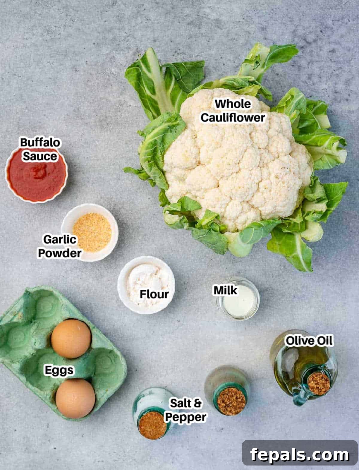 Collection of fresh ingredients for making cauliflower bites, including a head of cauliflower, eggs, milk, flour, garlic powder, and buffalo sauce.