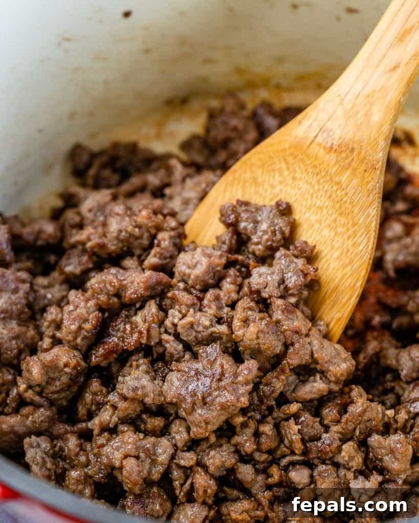 Hearty Unrolled Cabbage Soup 6 Ground beef perfectly browned in a Dutch oven with a wooden spoon, releasing rich aromas.