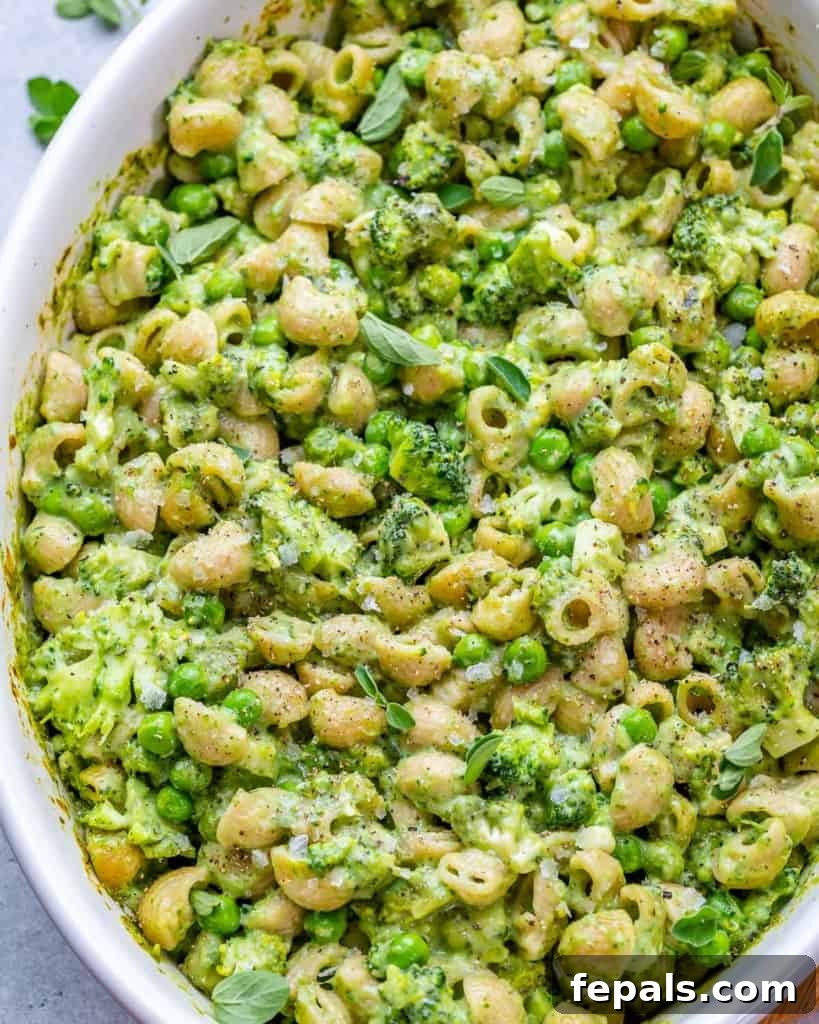 Close-up of creamy green mac and cheese with visible broccoli and peas.