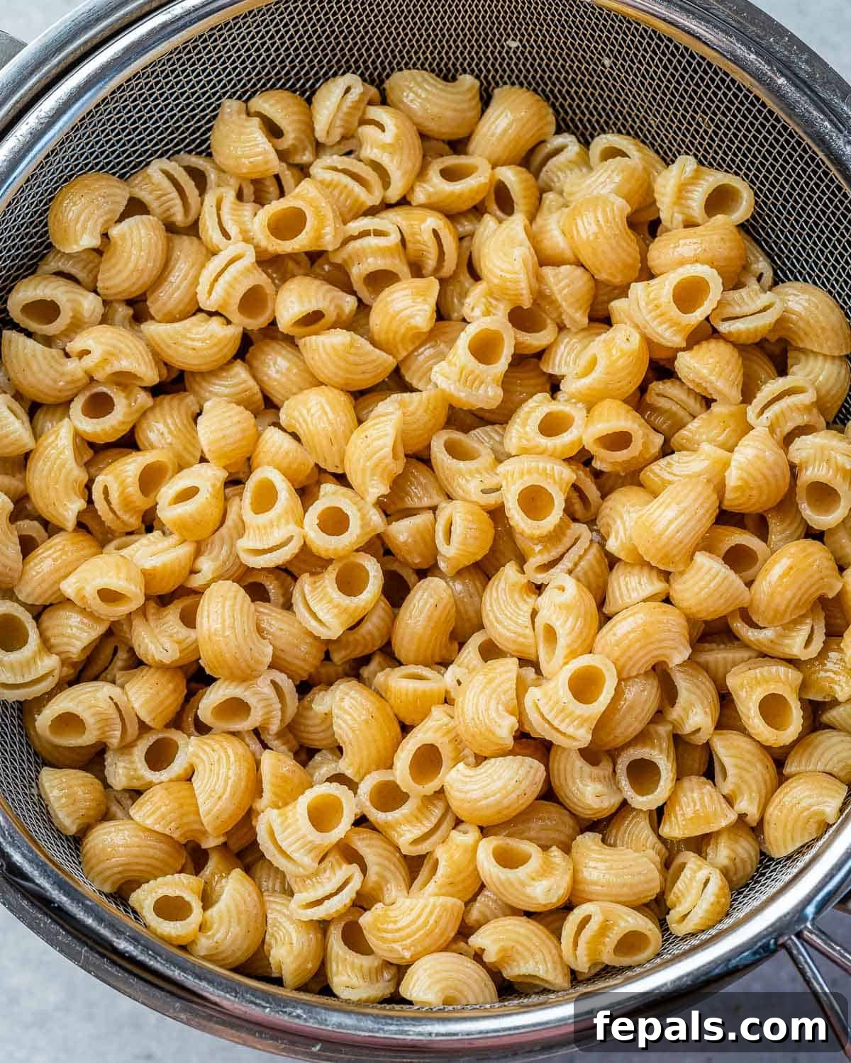 Boiled whole wheat pasta in a strainer, ready to be added to the baking dish.