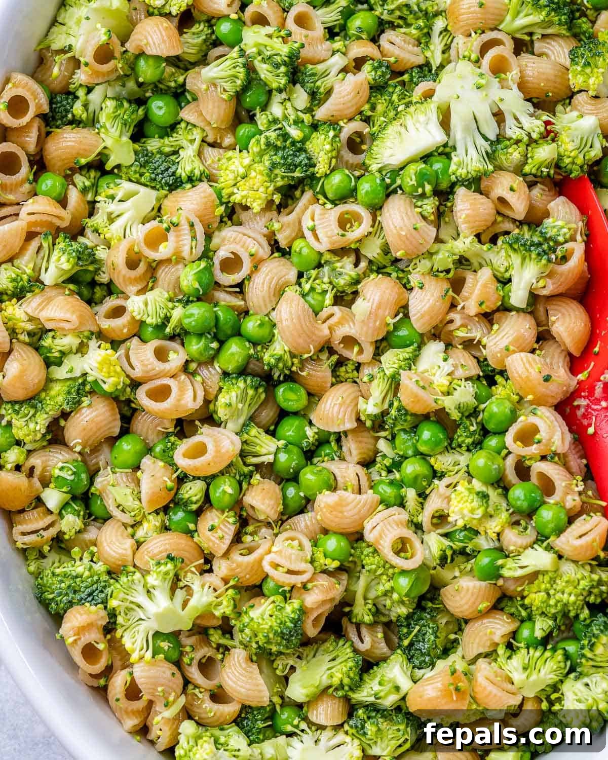 Boiled pasta, broccoli, and peas mixed together in a baking dish, awaiting the sauce.