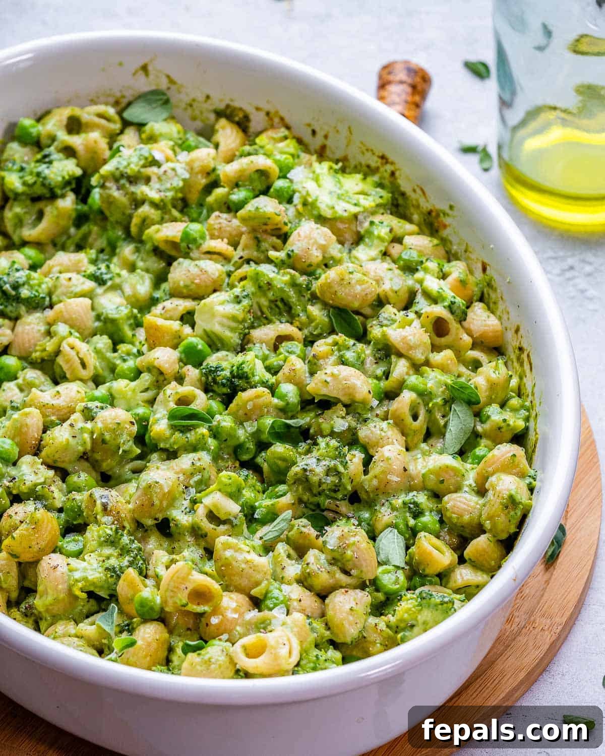 An oval baking dish filled with vibrant green mac and cheese, surrounded by fresh ingredients.