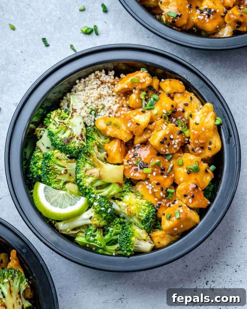 Top view of a single honey garlic chicken meal prep bowl with broccoli and quinoa, garnished with green onions and sesame seeds.