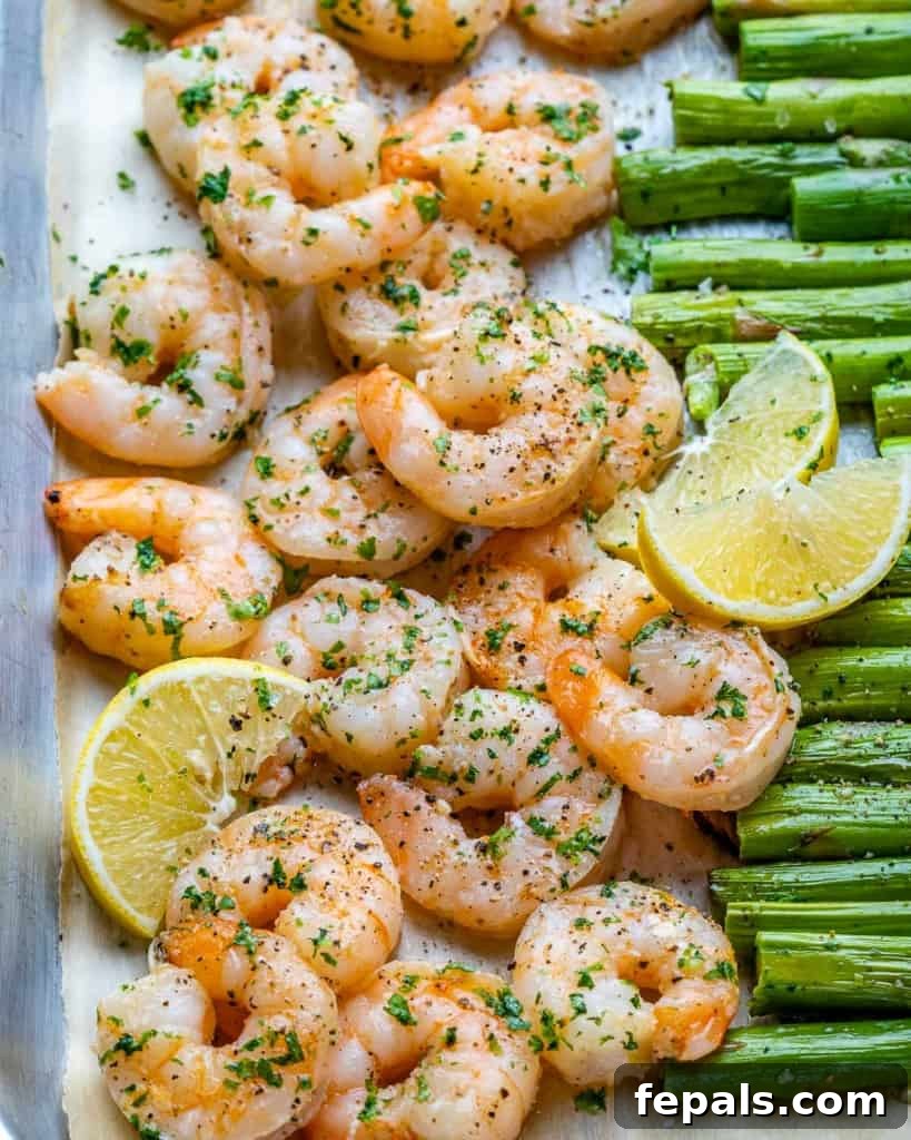 Roasted Garlic Shrimp & Asparagus Sheet Pan Dinner 3 Close-up shot of perfectly cooked, pink shrimp and bright green asparagus spears, speckled with minced garlic, on a sheet pan.