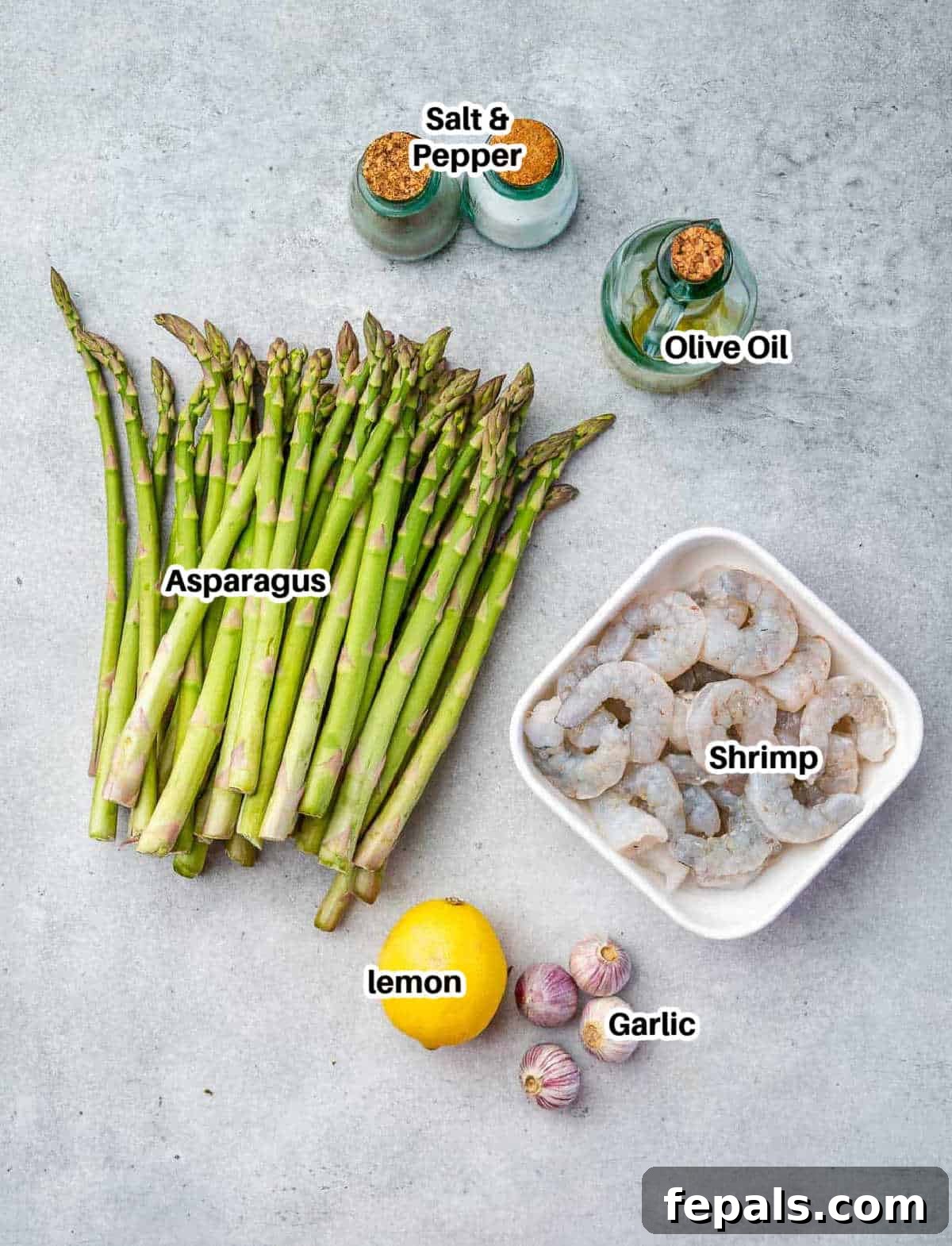 Roasted Garlic Shrimp & Asparagus Sheet Pan Dinner 4 A flat lay of ingredients for sheet pan asparagus and shrimp, including fresh asparagus, raw shrimp, garlic, lemons, and olive oil.