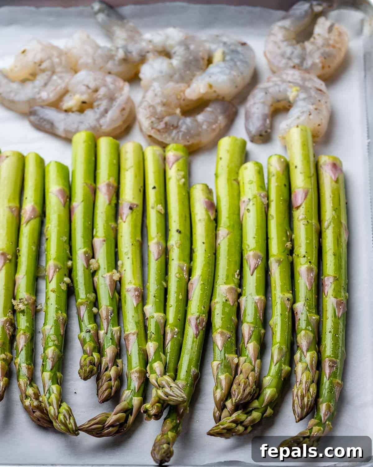Roasted Garlic Shrimp & Asparagus Sheet Pan Dinner 5 Raw asparagus and marinated shrimp are arranged neatly on a parchment-lined sheet pan, ready for baking.