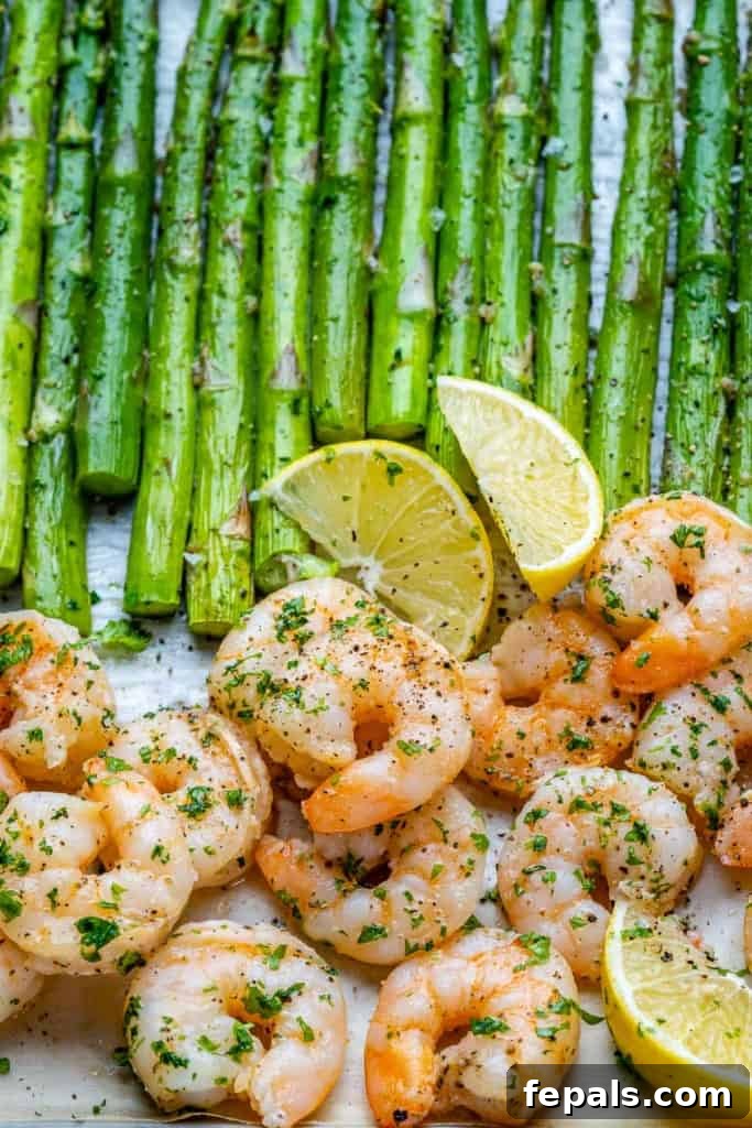 Roasted Garlic Shrimp & Asparagus Sheet Pan Dinner 9 A close-up view of a serving of sheet pan garlic shrimp and asparagus on a white plate, garnished with fresh herbs and lemon.