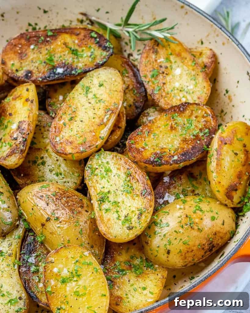 Crispy Garlic Skillet Potatoes 9 Side shot of pan-roasted garlic baby potatoes glistening with oil and herbs in a dark skillet.