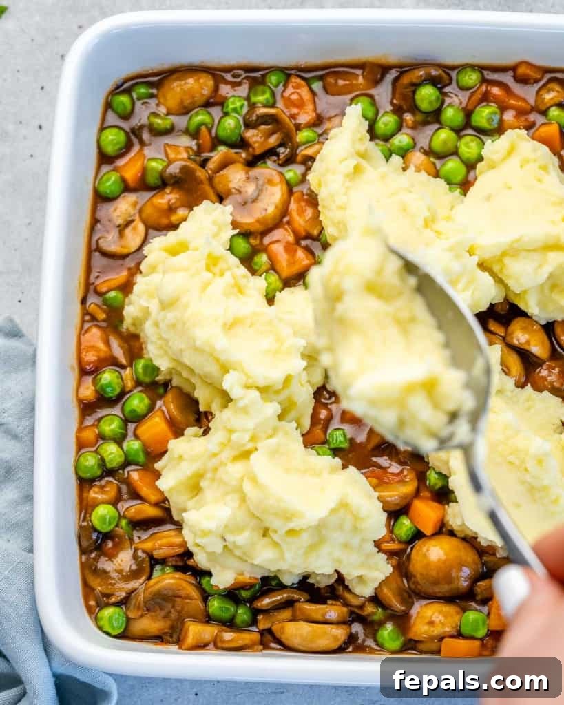 Garden Shepherd's Pie 6 A spoon delicately piling fluffy mashed potatoes on top of the rich vegetable filling in a baking dish.