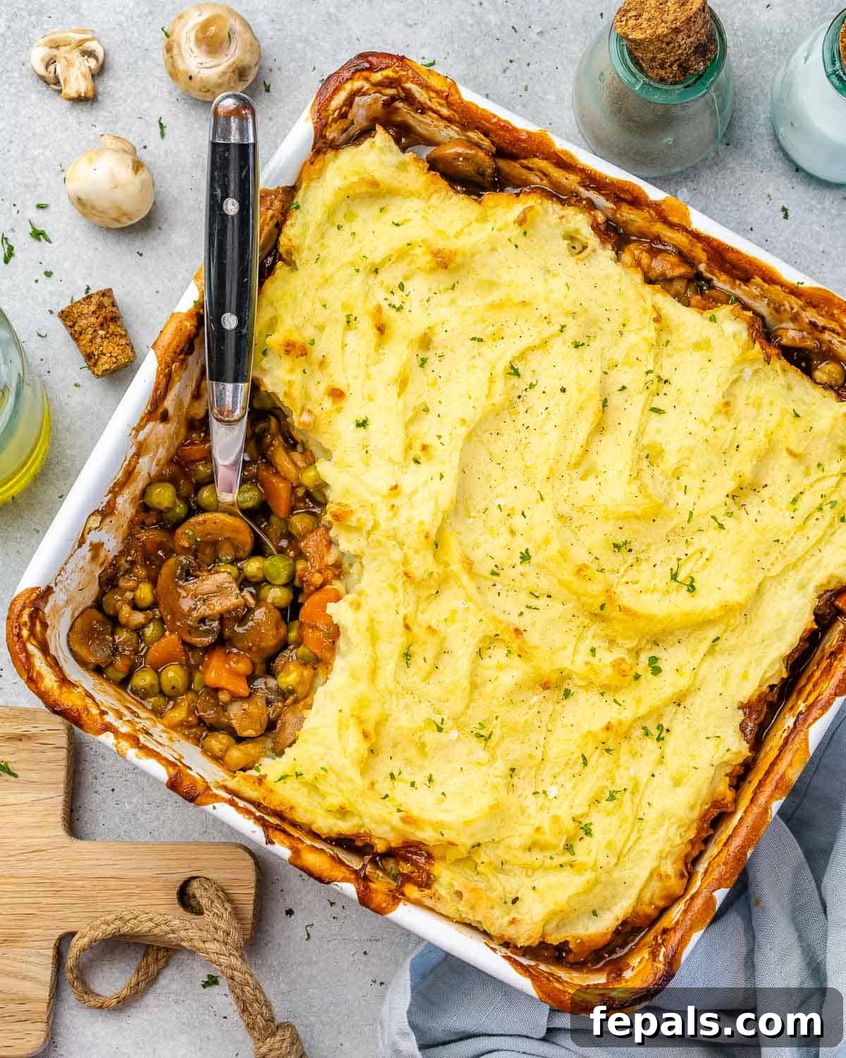 Garden Shepherd's Pie 7 Top view of a freshly baked vegetarian shepherd's pie, golden and bubbly, with kitchen ingredients subtly blurred in the background.