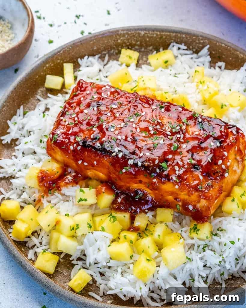 Fire-Kissed Salmon 8 Side shot of a flaky BBQ salmon fillet resting on a bed of rice, adorned with fresh pineapple chunks and a sprinkle of sesame seeds, ready to be enjoyed.