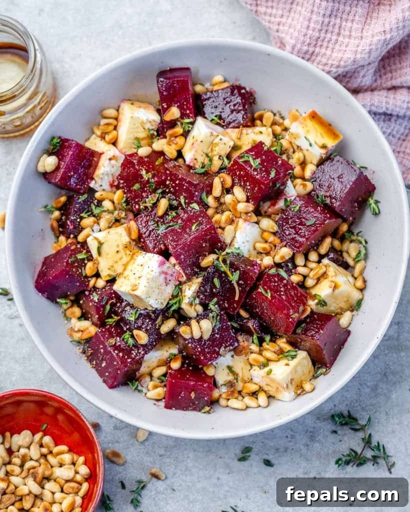 Vibrantly roasted beet salad in a white bowl, garnished with toasted pine nuts and fresh herbs, served on a pink linen cloth.