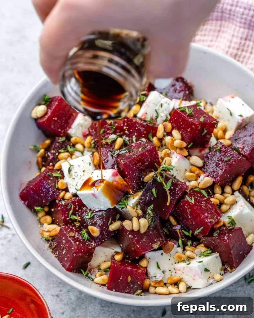 Rich balsamic vinaigrette being drizzled over a fresh roasted beet salad with feta and pine nuts in a pristine white bowl.