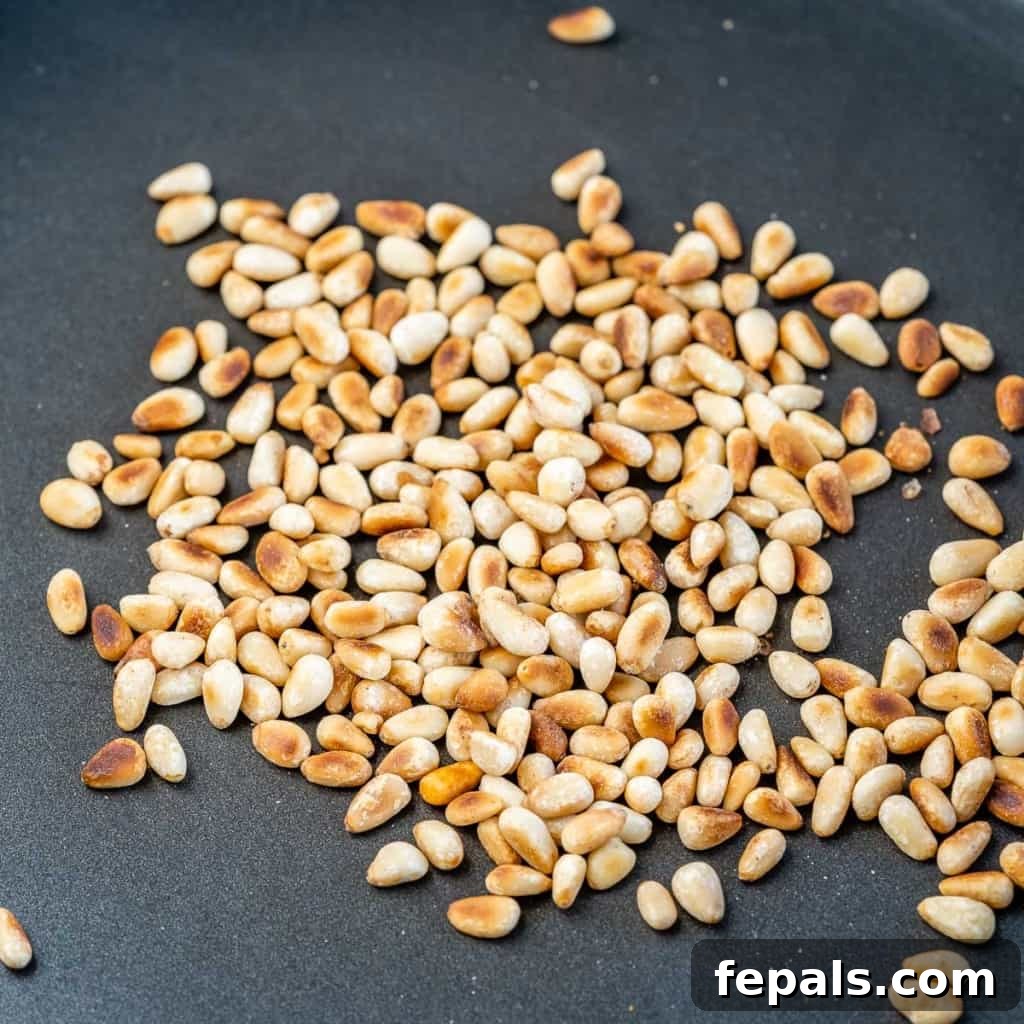 Golden brown toasted pine nuts scattered on a white surface, ready to be added to the salad.