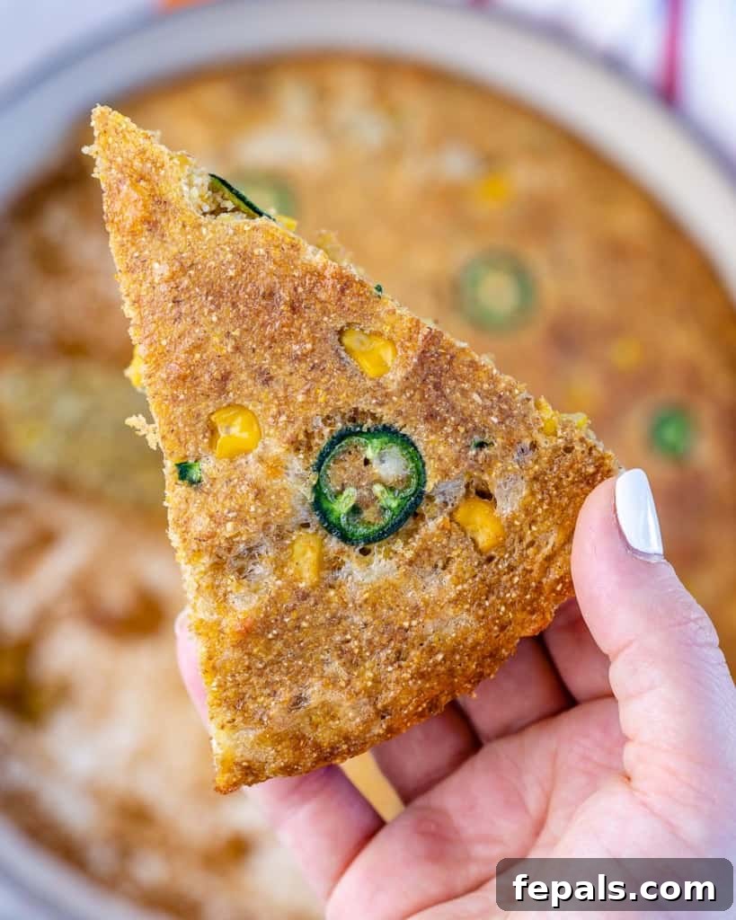 A single slice of Skillet Cornbread, perfectly cut, adorned with visible jalapeño and corn pieces.