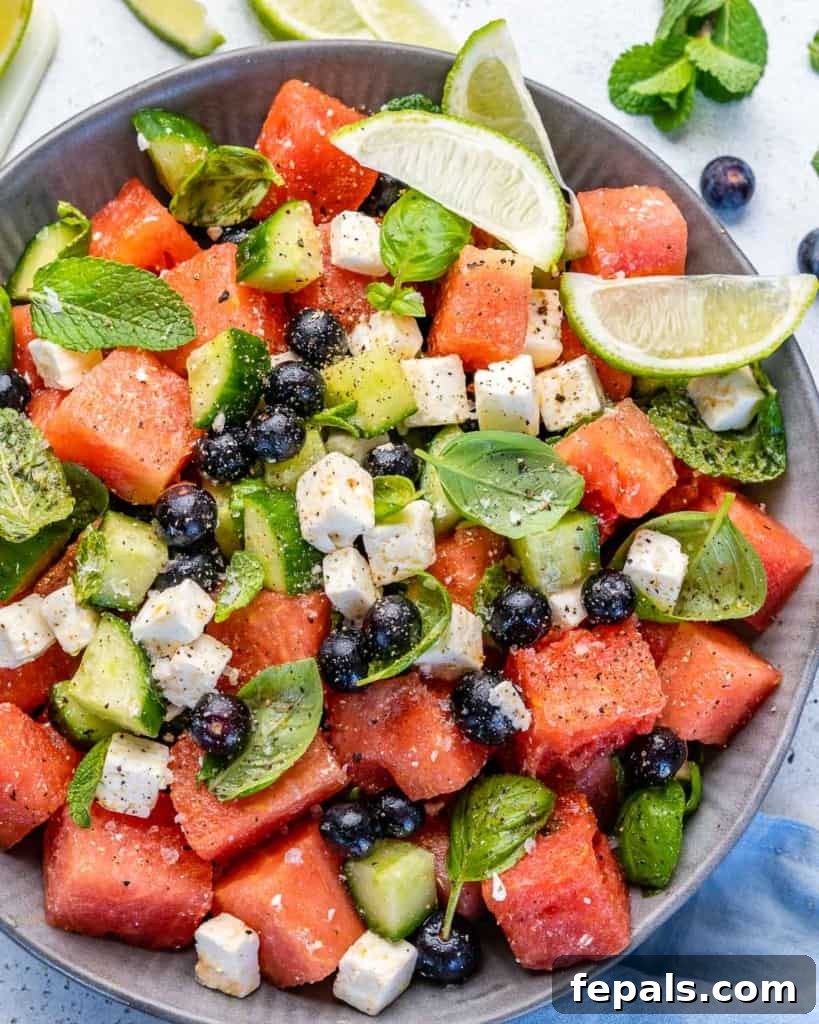 Vibrant Watermelon Feta Salad 2 Top view of a colorful watermelon feta salad in a rustic bowl, garnished with lime wedges and fresh mint leaves, ready to be served on a light background.