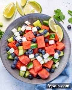 Top view of watermelon feta salad in grey bowl with lime wedges and fresh herbs