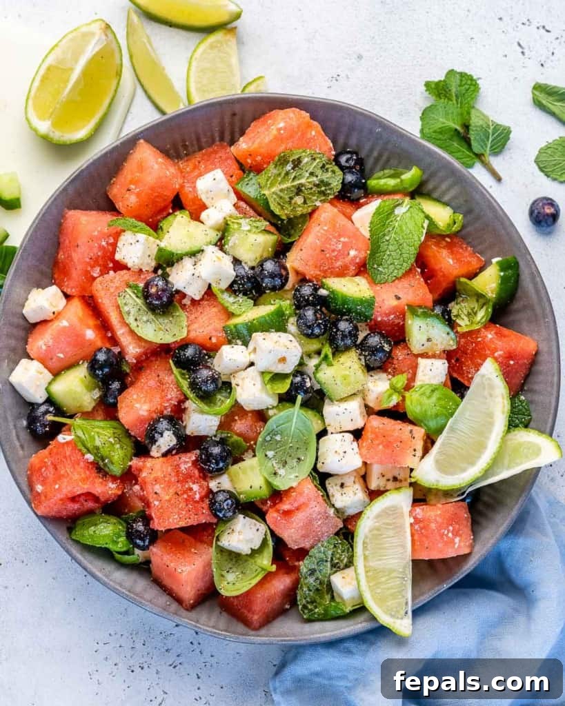 Vibrant Watermelon Feta Salad 3 Close-up top view of watermelon feta salad in a white bowl, showcasing the colorful ingredients: red watermelon, blue blueberries, white feta, and green herbs.
