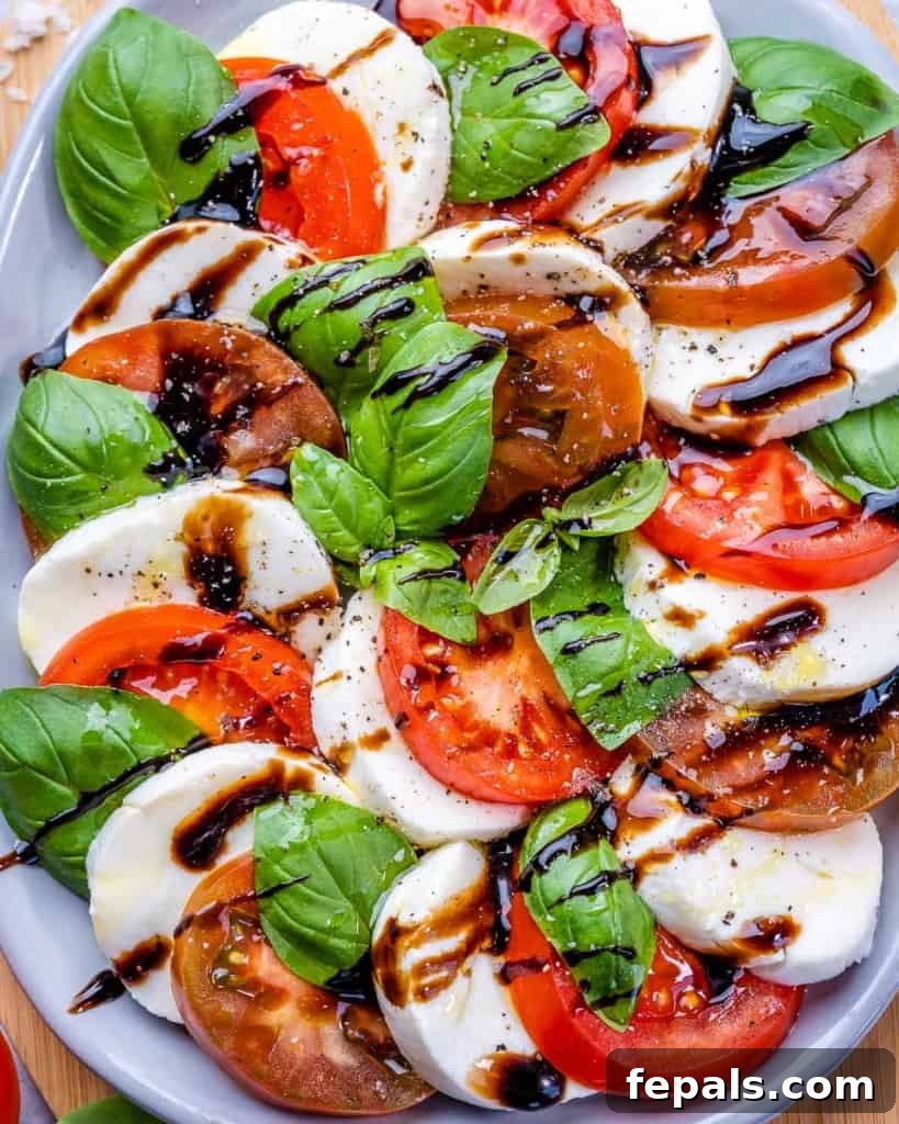 Effortless Caprese Perfection 3 Fresh Caprese salad beautifully arranged on a white plate, drizzled with balsamic glaze and adorned with vibrant green basil leaves.