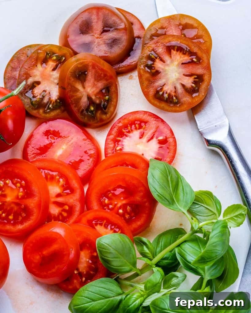 Effortless Caprese Perfection 5 Slices of ripe red tomatoes neatly arranged next to fresh green basil leaves, ready for assembling a Caprese salad.