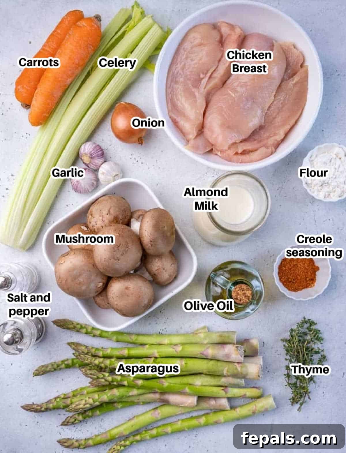 Velvet Chicken Supper 4 A selection of fresh ingredients laid out on a wooden surface, including chicken breasts, creole seasoning, olive oil, onions, carrots, celery, garlic, cremini mushrooms, thyme, gluten-free flour, almond milk, and asparagus, ready for making chicken fricassee.