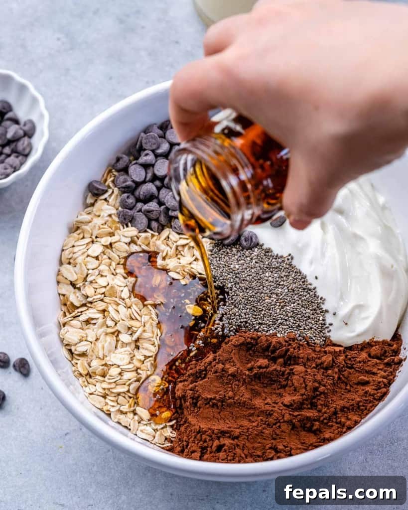 Sweet Dreams Chocolate Oats 6 oats, chocolate chips, cacao powder, chia seeds, yogurt, and maple syrup being poured in white bowl