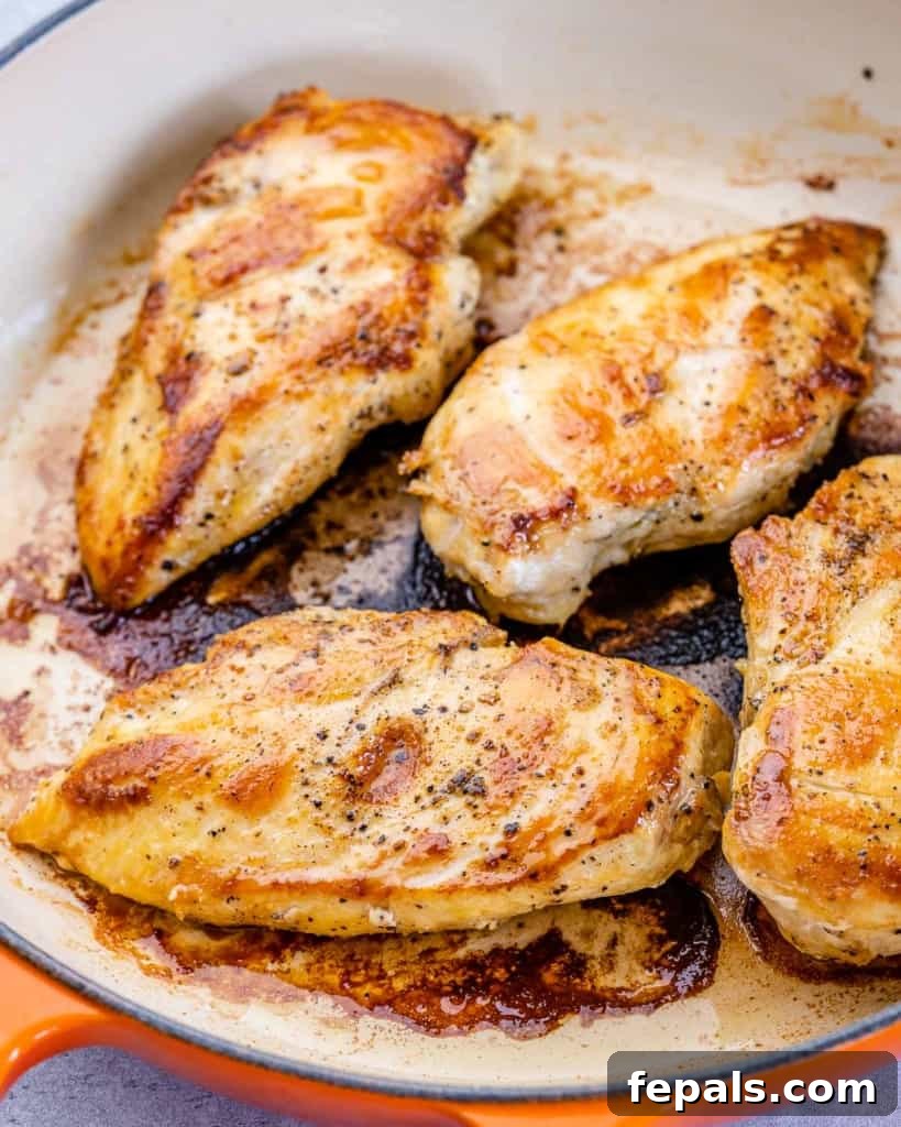 Four perfectly seared chicken breasts with a golden crust, resting on a plate after cooking.