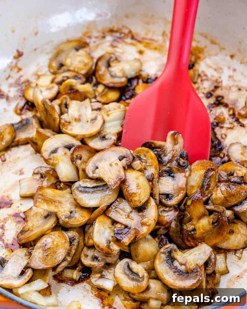 Sliced mushrooms being stirred in a hot skillet with a spatula, browning beautifully.