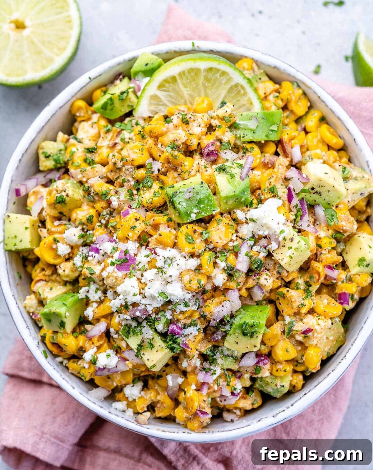 Zesty Fiesta Corn Salad 2 A beautifully presented Mexican street corn salad in a white bowl, garnished with fresh cilantro and a lime wedge, resting on a pink napkin.